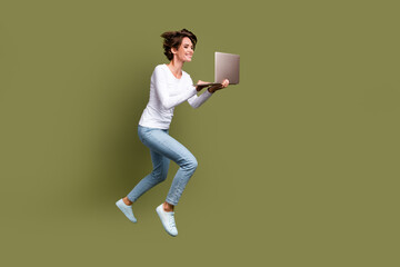 Fototapeta na wymiar Full size photo of attractive young woman hold netbook hurry running fast wear trendy white clothes isolated on khaki color background