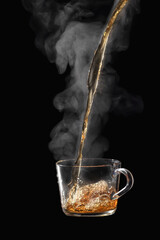 Process brewing tea on black background. Transparent glass cup of freshly brewed black tea steaming...