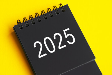 2025 black and white desk calendar on yellow cover background. New year concept