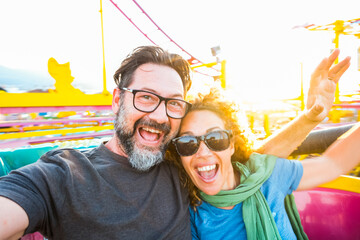 Adult couple have fun together on a roller coaster in amusement park taking selfie picture with the...