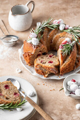 Christmas bundt cake decorated with glaze, cranberries and rosemary served on beige table. Homemade cake recipe