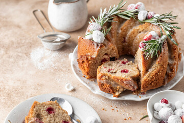 Christmas bundt cake decorated with glaze, cranberries and rosemary served on beige table. Homemade cake recipe