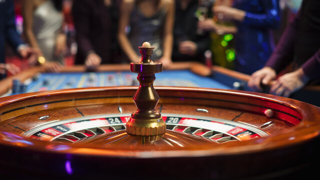 Close Up of a Spinning Roulette Wheel with the Ball Rolls Into a Black Pocket with Lucky Number. Casino Players Making Bets at a Roulette Table. Young People Enjoying Nightlife in a City
