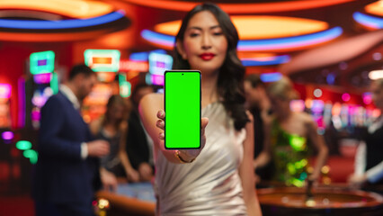 Modern Casino Setting: Gorgeous Asian Brunette Woman Posing with a Mobile Phone with a Green Screen...