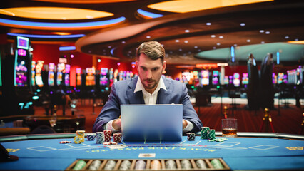 Portrait of a Happy Young Man in a Suit Using a Laptop Computer in Casino. Lucky Businessman...
