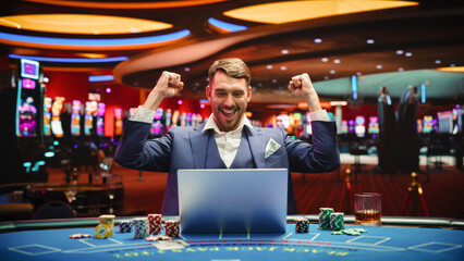Portrait of a Happy Young Man in a Suit Using a Laptop Computer in Casino. Lucky Businessman Celebrating and Cheering Blackjack Jackpot Win in Online Game on Betting Online Casino Website. 