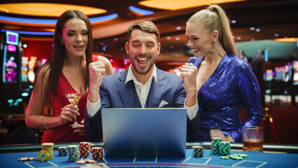 Portrait of a Happy Man with Two Female Partners Betting Online on a Laptop Computer while Sitting...