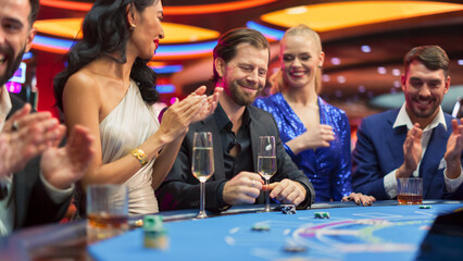 Portrait of a Newly Rich Man Winning at a Blackjack Table Card Game in a Modern Casino. Cinematic Shot of a Group of Exclusive Club Guests Celebrating a Lucky Bet and Victory