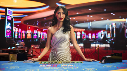 Portrait of a Profesional Asian Croupier in a Casino Dealing Playing Cards on a Baccarat Table. Game Dealer Opens and Reveals Winning Cards to the Audicence, Looking at the Camera in Online Casino - obrazy, fototapety, plakaty