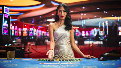 Portrait of a Profesional Asian Croupier in a Casino Dealing Playing Cards on a Baccarat Table. Game Dealer Opens and Reveals Winning Cards to the Audicence, Looking at the Camera in Online Casino - obrazy, fototapety, plakaty