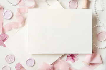 Card near pink decorations, seals and silk ribbons on white table top view, wedding mockup