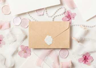 Obraz na płótnie Canvas Envelope near pink decorations, seals and silk ribbons on white table top view, wedding mockup
