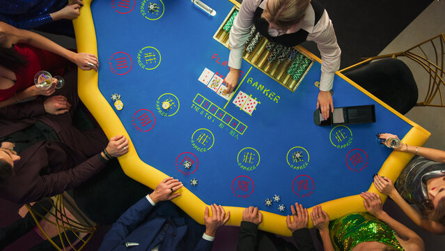 Top Down View Of Glamorous Casino Gamblers Placing Bets and Having Fun While Winning at Baccarat Table. Professional Croupier Dealing Cards, VIP People Enjoying Luxurious Lifestyle, Having Drinks.
