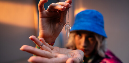 Close up of blonde woman holding and examining amethyst crystal on silver chain at neon studio light