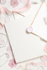 Card and envelope near pink decorations, seals and silk ribbons on white table top view, wedding mockup