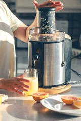 A woman makes orange juice at home in the kitchen with an electric juicer.