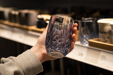 Woman holding glass from a shelf in homeware store.