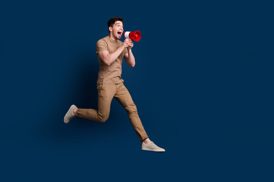 Full size photo of crazy man wear beige outfit running look at empty space sale screm in megaphone isolated on dark blue color background
