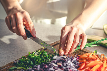Woman cutting and chopping onion by knife on wooden board.