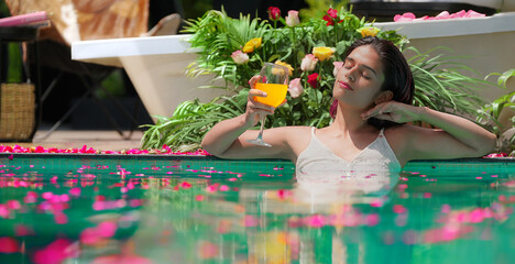 Indian Asian Hindu relax woman bathing rose petals water park pool edge resort hold glass drink...