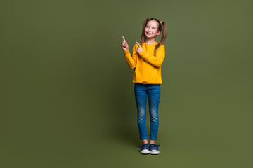 Full length photo of cute schoolgirl with ponytails wear yellow pullover look directing at empty...