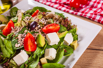 Spinach salad with avocado, feta cheese, tomatoes and seeds.