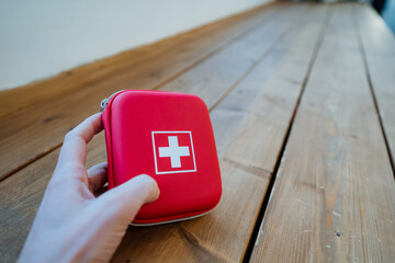 A hand holds a red first aid kit, a medical bag with medicines.