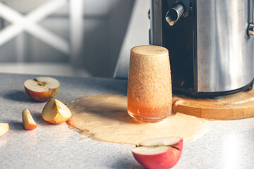 Juicer and glass filled with apple juice on the kitchen table.