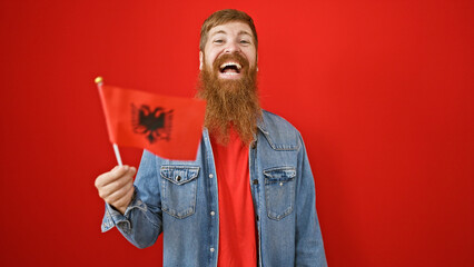 Cheerful young redhead guy, full of confidence, joyfully brandishing the albanian flag, poses over...