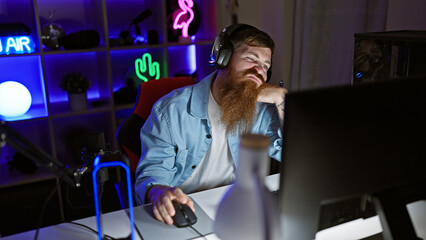 Bored young redhead man streamer getting tired, struggling to stay awake playing video game, engulfed in dark night in his gaming room