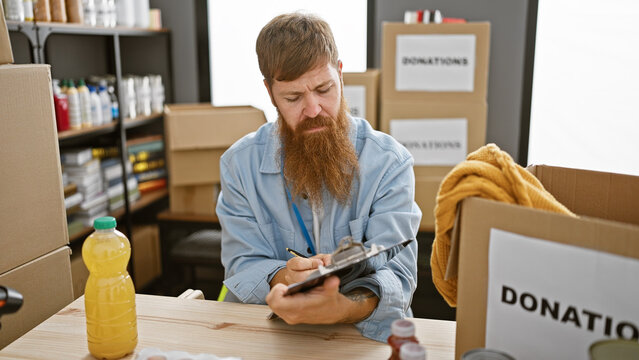 Diligent young redhead man volunteer taking notes at a charity center's table, offering social support with a relaxed beam