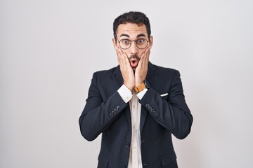 Handsome business hispanic man standing over white background afraid and shocked, surprise and amazed expression with hands on face