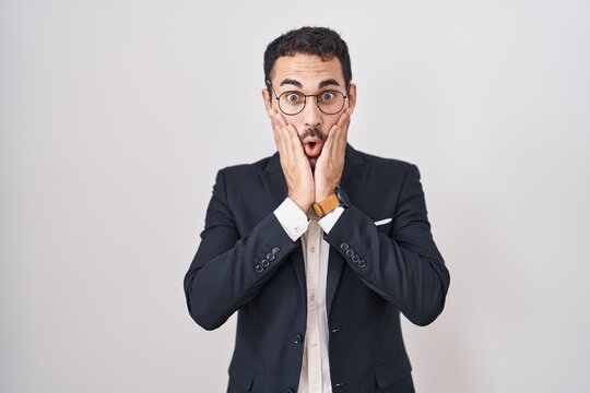 Handsome business hispanic man standing over white background afraid and shocked, surprise and amazed expression with hands on face