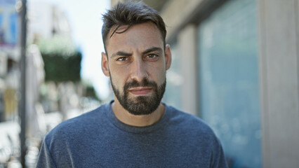 Young hispanic man standing with serious expression at street