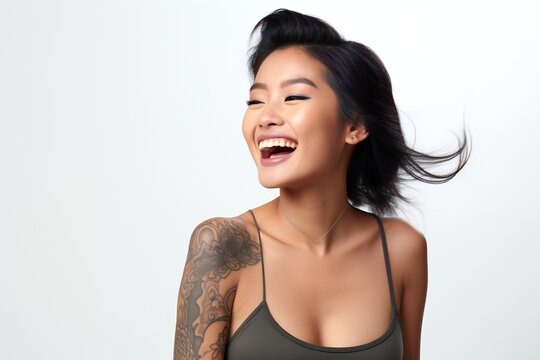 professional portrait studio photo of a handsome young asian american tatooed woman model with perfect clean teeth laughing and smiling. isolated on white background. for ads and web design