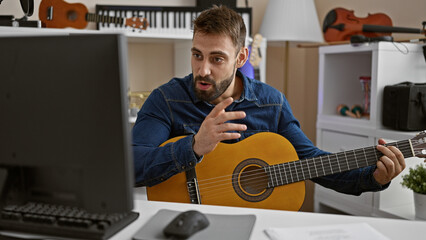 Handsome young hispanic man immersed in melody, strumming a classic guitar during online lesson in...