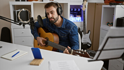 Handsome young hispanic man sitting in a music studio, passionately playing a chord on a classical...