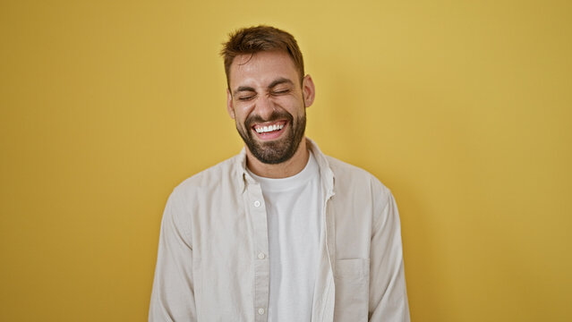 Joyful young hispanic man with beard, confidently laughing a lot in a stylish, casual fashion, standing against an isolated yellow background, enjoying life's vivid expressions.