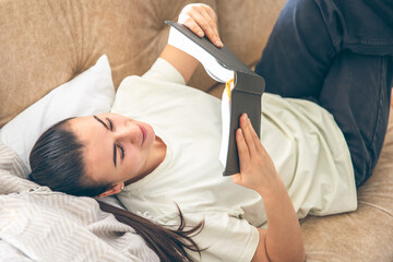 Obraz na płótnie Canvas A woman reads a book at home, lying on the sofa.