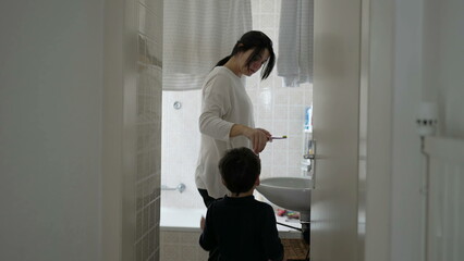 Candid mother and child standing in bathroom preparing to brush teeth together, domestic everyday...