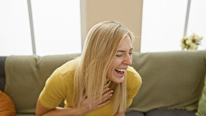 A young, joyful caucasian woman laughs in a cozy living room, portraying casual beauty and an inviting home atmosphere.