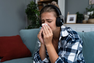 Young woman sitting at home listening to audio books or podcast on wireless headphones and crying....