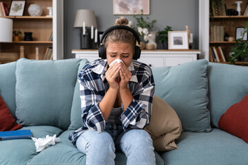 Young woman sitting at home listening to audio books or podcast on wireless headphones and crying. She feels sad and depressed about the subject they talking about.