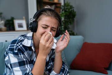 Young woman sitting at home listening to audio books or podcast on wireless headphones and crying....