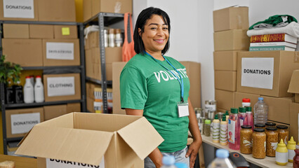 A smiling middle-aged hispanic woman volunteers sorting donations in a warehouse center.