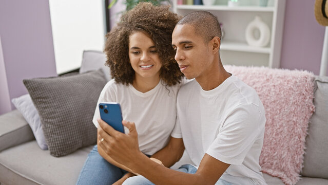 Beautiful couple enjoying fun lifestyle, sitting on sofa, making confident expressions, taking selfie picture with smartphone at home. smiling, joy-filled love together in their living room.