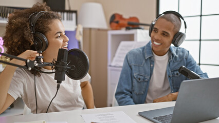 Working musicians donning headphones together at radio studio table, live on air, presenting music and news with smiles, professionalism, on a casual day. - obrazy, fototapety, plakaty
