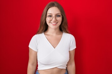 Young caucasian woman standing over red background with a happy and cool smile on face. lucky...