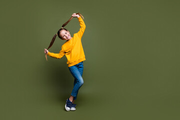 Full length photo of lovely kid dressed yellow sweatshirt holding her tails stand near empty space...