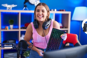 Young blonde woman playing video games holding keyboard winking looking at the camera with sexy...
